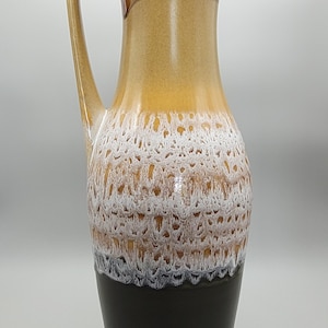 May include: A tall ceramic vase with a handle, showcasing a colour gradient. The top rim is light brown with a white, textured pattern. The middle section is a warm yellow, leading to a dark brown base. A decorative item for the home.
