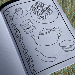 May include: Black and white line drawing of breakfast items on a page. Includes a cup of coffee, waffles, yogurt, a teapot, a banana, and a muffin. The word "COLAZIONE" is written vertically on the left side of the page.