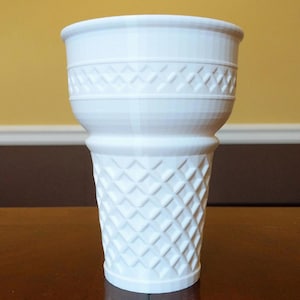 May include: A white plastic cup shaped like an ice cream cone, featuring a wide rim and a textured, diamond-patterned surface that mimics the appearance of a waffle cone. The cup has a tapered base and a smooth, flared upper section.
