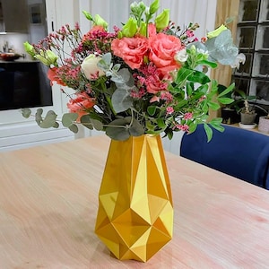 May include: A bouquet of pink and white flowers in a gold geometric vase. The vase is on a light wood table.