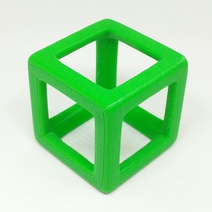 May include: A vivid green, open-frame cube, possibly 3D-printed, rests on a white surface. The cube's edges are smooth and well-defined, with a hollow centre. The geometric shape is a vibrant, solid colour, and the design is simple and modern.