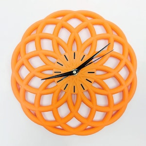 Può includere: Orologio arancione con un design geometrico e lancette nere. Il quadrante dell'orologio è di un'arancione più chiaro.