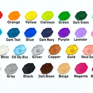 May include: A collection of colorful, hexagonal-shaped charms, each with a floral design. The charms are in various colors, including red, orange, yellow, green, blue, purple, and metallic shades like gold and silver. Each charm has a color name printed below it.