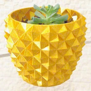 May include: A yellow geometric planter with a succulent plant. The planter has a textured surface with a repeating triangular pattern. The succulent has green leaves. The planter is designed to hold small plants.