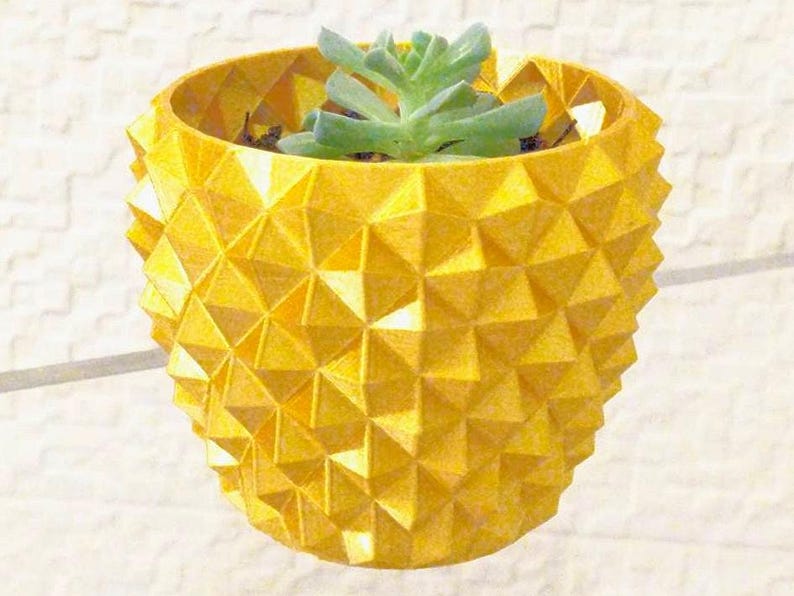 May include: A yellow geometric planter with a succulent plant. The planter has a textured surface with a repeating triangular pattern. The succulent has green leaves. The planter is designed to hold small plants.