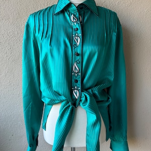 May include: A teal blue, long-sleeved button-up shirt with black and white embroidery. The shirt has a striped pattern and is tied at the waist.