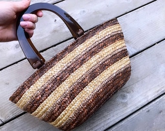 Puede incluir: Un bolso tote tejido a rayas marrones y beige con un asa de plástico marrón oscuro.