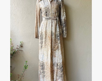 May include: A long-sleeved maxi dress with a floral print in shades of brown, white, and black. The dress has a collared neckline, a button-up front, and a tie belt at the waist.