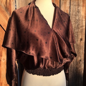 May include: A brown satin blouse with a ruffled neckline and a gathered elastic waistband. The blouse has a small, repeating pattern of black floral designs.