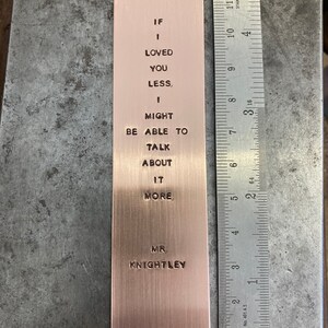 May include: A copper bookmark with the text "If I loved you less, I might be able to talk about it more. Mr. Knightley" engraved on it.