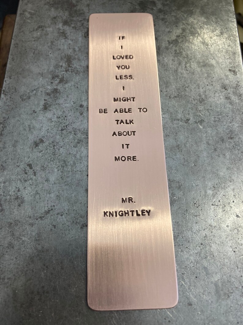 May include: A copper bookmark with the quote "If I loved you less, I might be able to talk about it more." inscribed on it. The quote is attributed to Mr. Knightley.