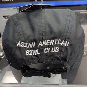 May include: Black baseball cap with a white embroidered logo that reads "ASIAN AMERICAN GIRL CLUB".