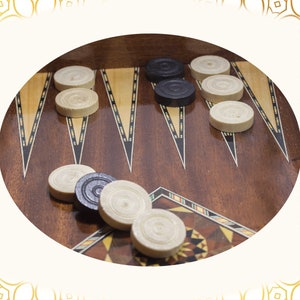 May include: A close-up of a backgammon board with white and black checkers. The board is made of wood and has a dark brown finish. The checkers are arranged in a pattern on the board.