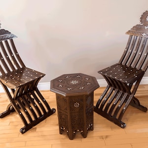 Puede incluir: Dos sillas de madera tallada con una mesa octogonal a juego. Las sillas y la mesa tienen un acabado marrón oscuro y diseños florales intrincados con detalles de nácar.