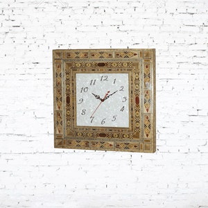 May include: A square clock with a white face and black hands. The clock is surrounded by a decorative frame made of inlaid wood and mosaic tiles in shades of brown, gold, and red.
