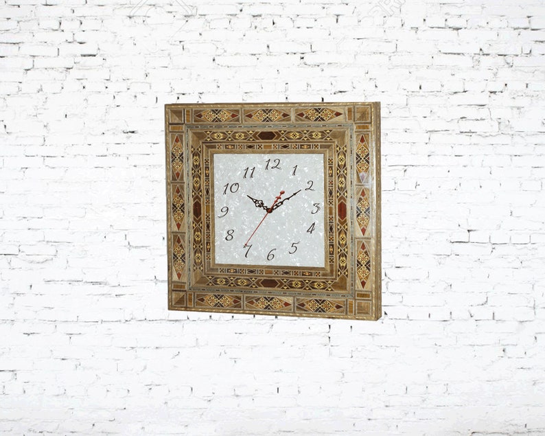 May include: A square clock with a white face and black hands. The clock is surrounded by a decorative frame made of inlaid wood and mosaic tiles in shades of brown, gold, and red.