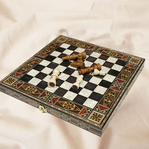 May include: A wooden chessboard with inlaid designs in shades of brown, red, and gold. The board is open and shows a game in progress with white and brown chess pieces.