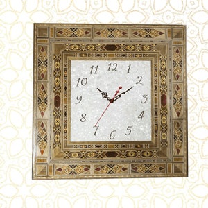 May include: A square clock with a white face and black Roman numeral hour markers. The clock is framed in a decorative wooden frame with intricate inlaid wood patterns in shades of brown, beige, and red.