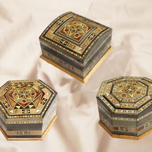 May include: Three decorative wooden boxes with detailed geometric designs. The boxes display a variety of light and dark wood shades, with yellow and brown highlights. The boxes are in different shapes, including a curved top and two octagonal shapes.