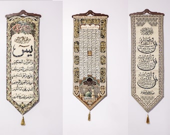 May include: Three vertical fabric wall hangings featuring intricate Arabic calligraphy and decorative borders. Each piece is suspended from a dark wooden rod and finished with a gold tassel at the pointed bottom edge, displaying detailed woven patterns.