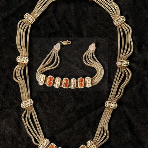 May include: A gold necklace and bracelet set with multiple strands of chain and orange gemstone accents.