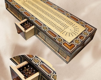 May include: A wooden cribbage board with an intricate inlaid design. The board has a drawer that opens to reveal a set of pegs.