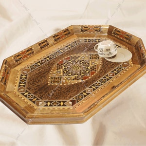Puede incluir: Bandeja octogonal de madera con intrincados patrones geométricos incrustados en varios tonos de marrón. Una pequeña taza y un platillo blancos con la palabra "Coffee" impresa en la taza se colocan en la bandeja.