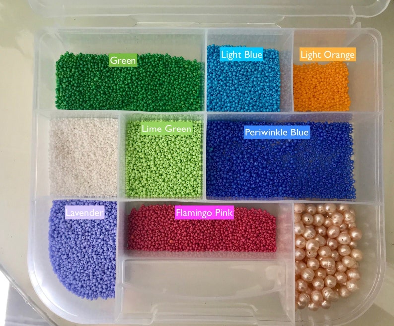 May include: A clear plastic storage box with compartments filled with various colours of small round beads. The compartments are labelled with the colour of the beads: Green, Light Blue, Light Orange, Lime Green, Periwinkle Blue, Lavender, Flamingo Pink. The last compartment contains larger, round, pearl-like beads.