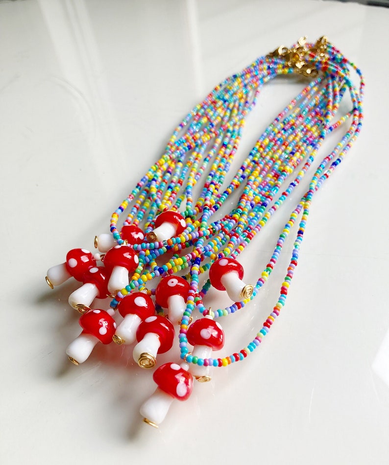 May include: A colourful beaded necklace with multiple red and white mushroom charms. The necklace is made of small, colourful beads and has a gold clasp.