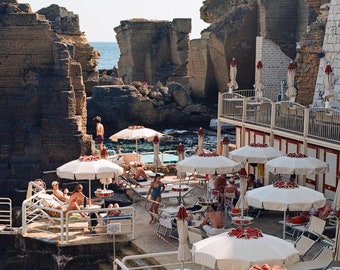 Puede incluir: Una escena junto a la piscina con sombrillas blancas y sillas, con un fondo de acantilados rocosos. La piscina es visible en el fondo, y el agua es de un azul turquesa.