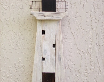 May include: A whitewashed wooden lighthouse with a black roof and a yellow window. The lighthouse is on a blue and brown base that resembles water.