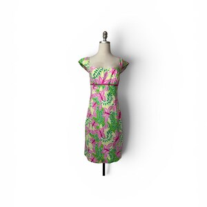 May include: A knee-length dress featuring a vibrant pattern of pink butterflies and green leaves on a light yellow background. The garment has short cap sleeves, a square neckline, and a solid dark pink horizontal band at the waistline.