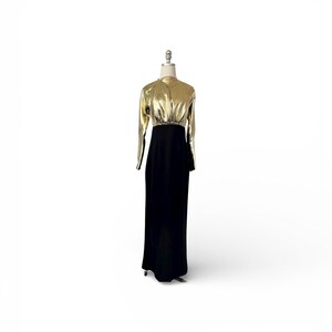 May include: A formal, floor-length gown with a gold metallic bodice and long sleeves. The skirt is black and flows to the floor. The dress is displayed on a mannequin against a white background.