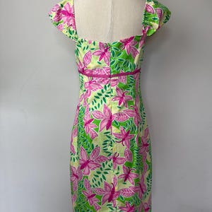 May include: A knee-length dress featuring a vibrant pattern of pink butterflies and green leaves on a pale yellow background. The garment has short cap sleeves, a square neckline, and a horizontal pink band accenting the waistline area.