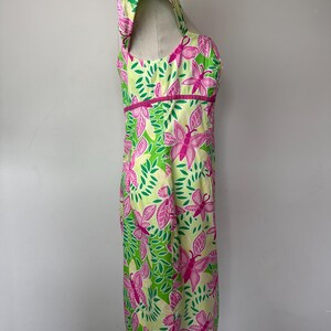 May include: A sleeveless dress featuring a vibrant pattern of pink butterflies and green leaves on a pale yellow background. The dress has a square neckline, a fitted bodice with a horizontal pink band at the waist, and a straight skirt silhouette.