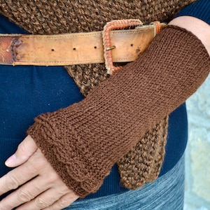 Puede incluir: Calientamanos de punto marrón con textura de canalé. Los calientamanos se llevan sobre una camisa azul y un chal de punto marrón.