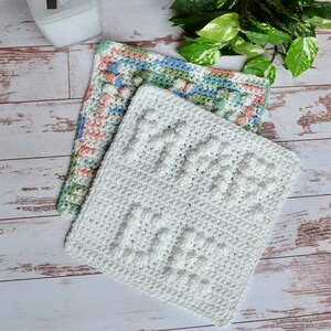 May include: Two handmade crochet washcloths. One is white with a textured pattern, and the other is multi-colored with pink, blue, and green hues. The washcloths are square and appear to be made of soft yarn.