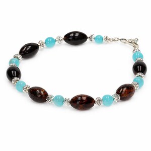 May include: A bracelet with black, brown, and turquoise beads. The bracelet has a silver clasp and small, sparkling accents between the beads. The oval and round beads create a unique jewellery design.