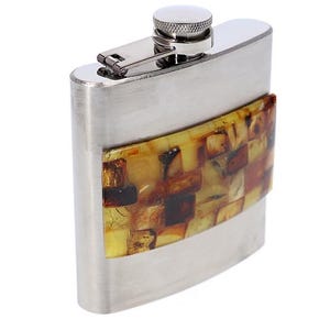 May include: A stainless steel hip flask with a curved rectangular design. It has an amber-coloured mosaic panel and a hinged cap with a screw-on top. The flask is designed for carrying liquids, such as spirits.