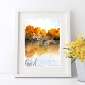 Puede incluir: Pintura acuarela de un lago con &aacute;rboles en el fondo. Los &aacute;rboles son una mezcla de naranja, amarillo y marr&oacute;n. El lago es de color azul claro con un reflejo de los &aacute;rboles en el agua.