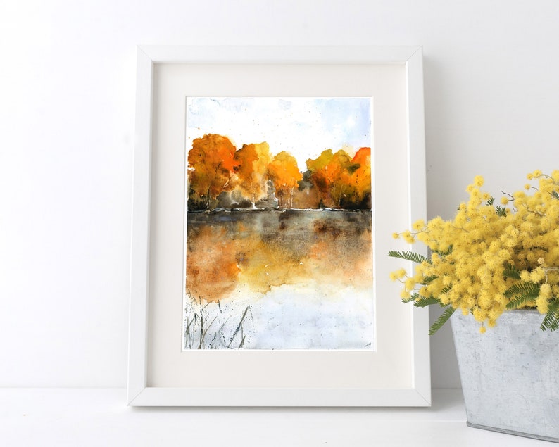Puede incluir: Pintura acuarela de un lago con &aacute;rboles en el fondo. Los &aacute;rboles son una mezcla de naranja, amarillo y marr&oacute;n. El lago es de color azul claro con un reflejo de los &aacute;rboles en el agua.
