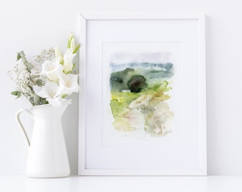Op de afbeelding: Een ingelijste aquarel landschapsschilderij met een witte rand. Het kunstwerk toont een groen en geel veld, een donkergroene boom en een nevelige blauwe en paarse lucht. Een witte kan met witte bloemen staat links.