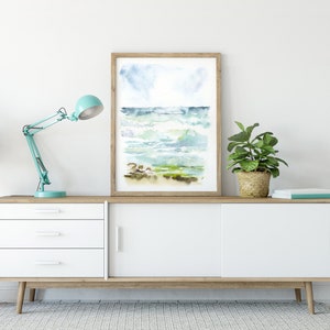 May include: A white dresser with three drawers and two sliding doors. A blue desk lamp is on the left side of the dresser. A potted plant is on the right side of the dresser. A framed watercolor painting of a seascape is above the dresser.