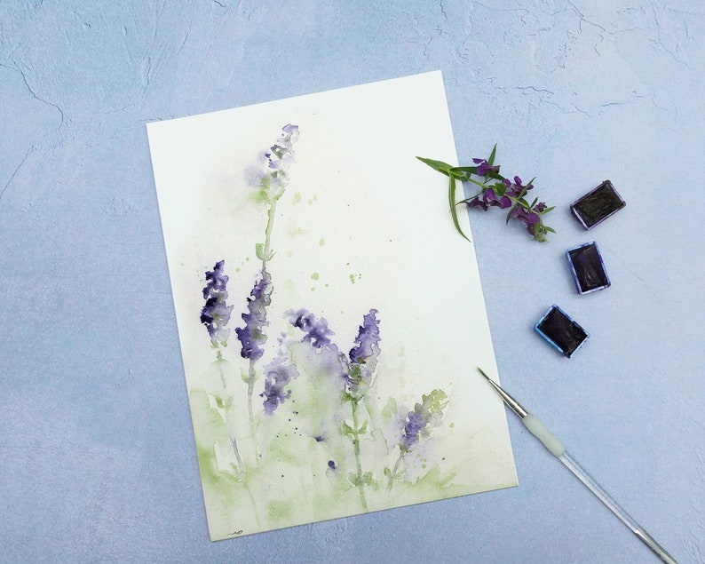 K&ouml;nnte beinhalten: Ein Aquarellbild von Lavendelbl&uuml;ten auf wei&szlig;em Papier. Das Bild ist von Aquarellfarben und einem Pinsel umgeben.