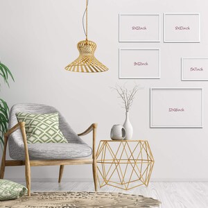May include: A white wall with five white picture frames of different sizes. The frames are hanging on the wall. The frames are labeled with their dimensions in inches. A gold geometric side table with a white vase and a gold pendant light are in the foreground.