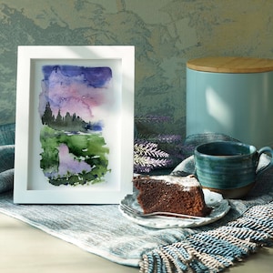 Pode incluir: Uma pintura em aquarela emoldurada retrata uma paisagem com um c&eacute;u roxo e rosa, campos verdes e &aacute;rvores escuras. Uma caneca de cer&acirc;mica azul, uma fatia de bolo de chocolate em um prato pequeno e um recipiente azul com tampa de madeira tamb&eacute;m est&atilde;o presentes.