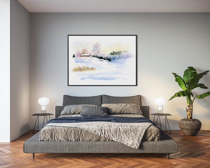 May include: A watercolor painting of a snowy landscape with a small house in the distance. The painting is framed in black and hanging on a gray wall above a gray bed with a gray blanket and pillows. There are two white lamps on black side tables next to the bed. A potted plant is on the right side of the image.