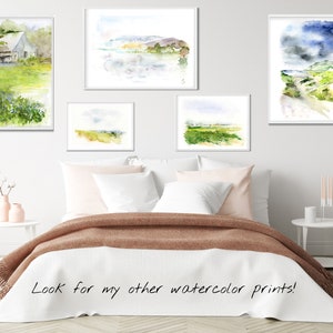 May include: Five watercolor paintings of landscapes, including a farmhouse, a lake, a field, and a path, are displayed on a white wall above a bed with a brown blanket.
