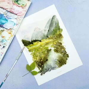 Pu&ograve; includere: Un dipinto ad acquerello di un paesaggio montano con un campo verde in primo piano. Le montagne sono dipinte in tonalit&agrave; di grigio e blu, e il campo &egrave; di un verde vibrante con sfumature di giallo. Il dipinto &egrave; realizzato su uno sfondo di carta bianca.