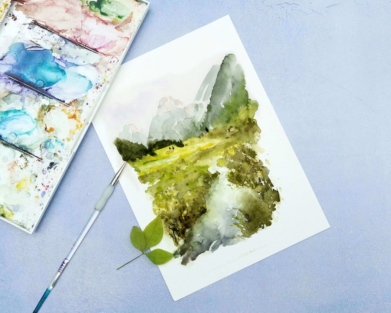 Pu&ograve; includere: Un dipinto ad acquerello di un paesaggio montano con un campo verde in primo piano. Le montagne sono dipinte in tonalit&agrave; di grigio e blu, e il campo &egrave; di un verde vibrante con sfumature di giallo. Il dipinto &egrave; realizzato su uno sfondo di carta bianca.